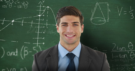 School scene with young Caucasian male smiling in front of a chalkboard. He has short brown hair,...