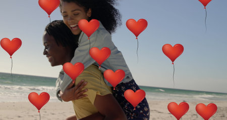 Image of red heart balloons floating over man giving piggyback ride to woman at beach. Happy...