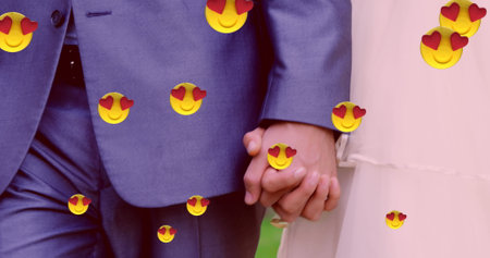 Image of multiple heart eyes face emoji floating against mid section of newly married couple holding hands. Happy Valentines Day celebration concept digitally generated image.の写真素材