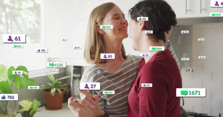 Image of social media icons and numbers over lesbian caucasian couple at home. Global social media, data processing and digital interface concept digitally generated image.の写真素材