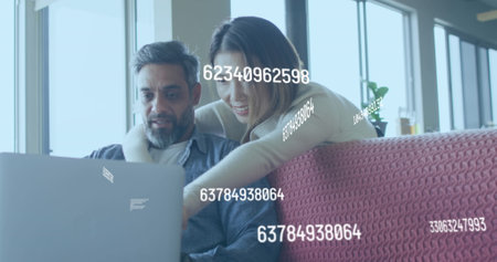 A couple is sitting in a living room using a laptop and talking. They are spending quality time at...