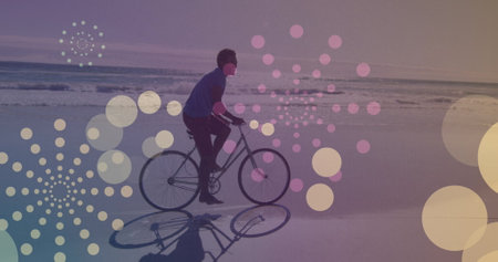 Yellow spots of light floating against african american man riding a bicycle at the beach. pedal day...