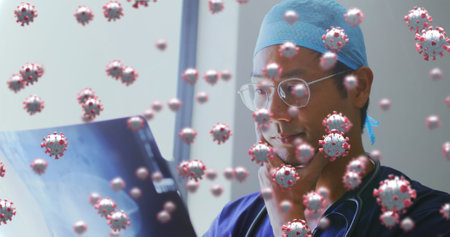 Image of a male doctor examining x-ray picture in hospital with coronavirus cells floating on the...