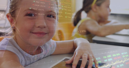 Caucasian female child sitting at desk, holding smartphone. She has light brown hair, blue eyes, and is wearing pink topの写真素材