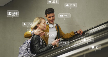 Image of social media icons floating over happy diverse couple embracing on moving stairs. social media and communication interface concept digitally generated image.の写真素材