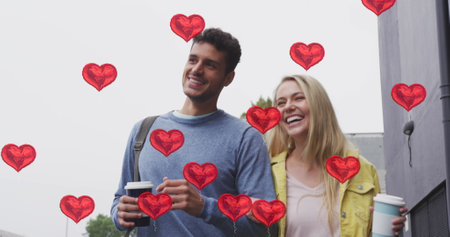 Image of heart icons floating over happy caucasian couple walking and drinking takeaway coffee. social media and communication interface concept digitally generated image.の写真素材