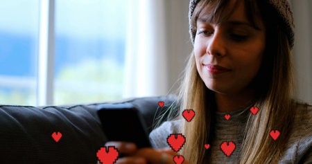 Digital composite of a Caucasian woman sitting on a couch while texting and digital hearts flying in...