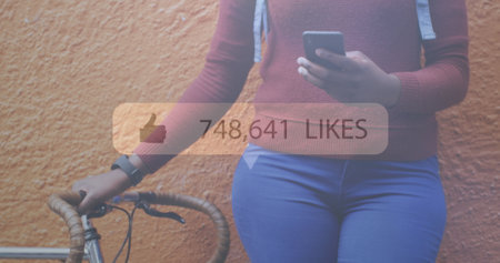 Image of social media notification over african american woman with bike using smartphone. global communication technology and social network concept digitally generated image.の写真素材
