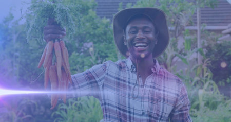 Image of blue lights over smiling african american man holding carrots. Community garden week digitally generated image.の写真素材