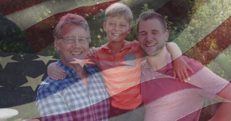 Image of flag of usa waving smiling caucasian grandfather, father and grandson. american patriotism, independence and celebration concept digitally generated image.の写真素材