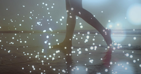 Glowing blue spots of light against low section of a woman walking on the beach. Love and relationship conceptの写真素材