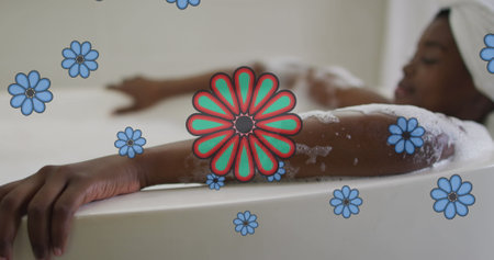 Image of blue flowers over happy african american woman relaxing in bath at home. relaxation, health and wellbeing concept digitally generated image.の写真素材