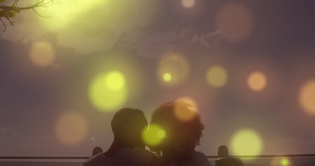 Glowing spots of light falling against african american couple kissing each other at the beach. Love and relationship conceptの写真素材