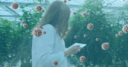 Image of coronavirus cells flowing over a female laboratory worker examining plants in the...