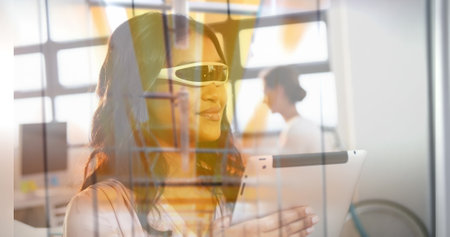 Biracial young adult holding tablet, looking through window. She has long dark hair, light brown skin, and wearing sunglassesの写真素材