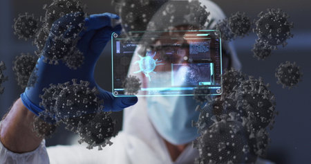 Image of covid 19 cells over scientist in ppe suit holding screen with medical data processing. global coronavirus pandemic, medicine and research concept digitally generated image.の写真素材