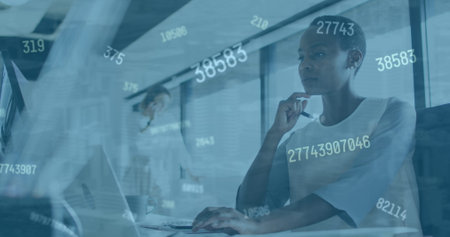 Image of numbers changing over afrcan american woman with computer in office. Business, finance,...