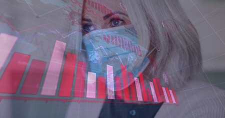 Caucasian healthcare worker wearing mask is looking at graphs. She has grey hair, blue eyes, and is...