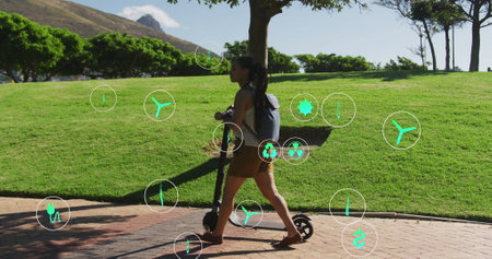 Image of ecology icons over biracial woman walking with scooter in park. health and fitness concept digitally generated image.の写真素材