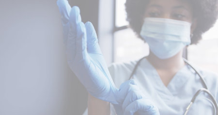 Image of covid 19 cells with female doctor wearing mask putting on gloves. healthcare and protection during coronavirus covid 19 pandemic, digitally generated image.の写真素材