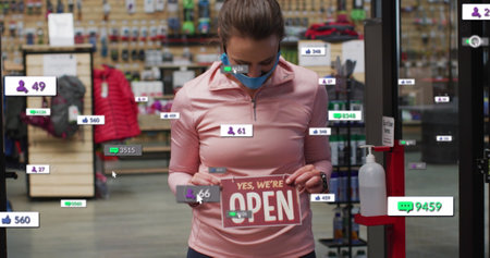 Image of media icons over caucasian female worker with face mask opening shop. social media and...