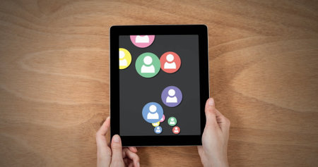 Hands clutch tablet showing vibrant social media icons. Wooden table provides simple background for...