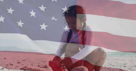 Image of flag of united states of america over biracial girl playing with sand on beach. American patriotism, diversity and tradition concept digitally generated image.の写真素材