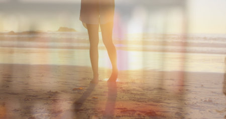 Image of a Caucasian woman wearing a face mask, looking at the camera over Caucasian woman standing on a beach, taking a selfie. Coronavirus Covid-19 pandemic concept digital compositeの写真素材