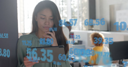 Processing data over happy biracial casual businesswoman using tablet at office. Casual business, data, digital interface, connection, office and communication digitally generated image.の写真素材