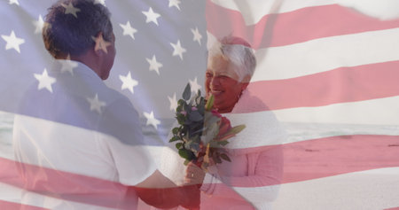 Image of flag of united states of america over senior biracial couple with flowers on beach. American patriotism, diversity and tradition concept digitally generated image.の写真素材