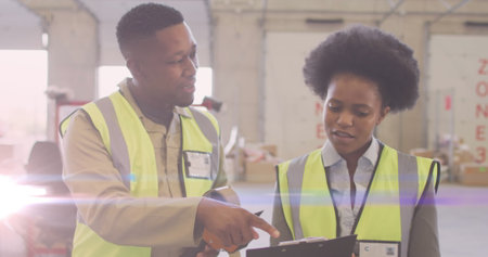 Image of glowing light over african american man and woman working in warehouse. labor day, work, workers, tradition and celebration concept digitally generated image.の写真素材