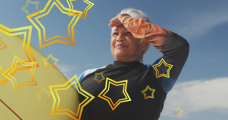 Senior biracial woman shields her eyes from the sun outdoors. She appears confident and adventurous,...