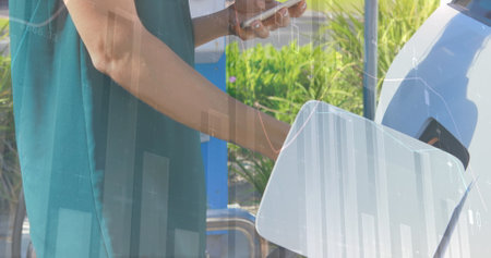 Close up of a woman typing on her phone while filling up on gas. Digital image of graphs and...