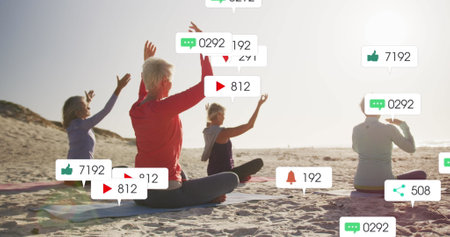 Image of social media notifications, over women doing yoga on beach. positive feelings and wellbeing social media concept, digitally generated image.の写真素材