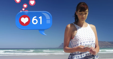 Close up of a Caucasian woman texting on the beach on a sunny day. Beside her in the foreground is a...