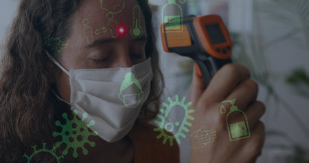 Image of covid 19 icons over woman wearing face mask. global covid 19 pandemic and vaccination...