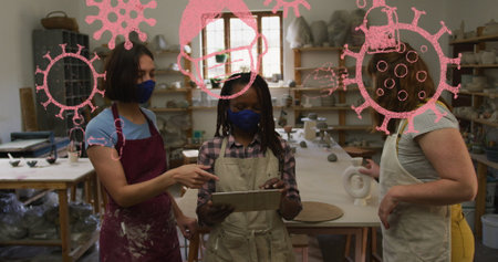 Image of covid 19 cells and icons over women wearing face masks in pottery workshop. global covid 19...