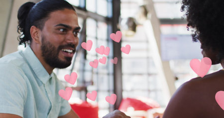 Pink heart icons against african american couple holding hands while sitting in a restaurant. love and relationship conceptの写真素材