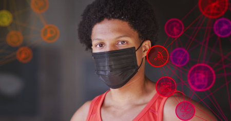 Image of media icons over african american man with face mask. Global business and digital interface...