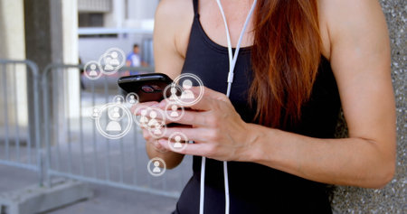 Digital composite of the half body of a young adult woman from her torso to her head. She is listening to her phone with her headset on while a series of vector icons of people appearing on the screen 4kの写真素材