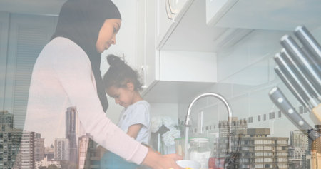 Image of asian mother with daughter in kitchen over cityscape. family spending free time together,...