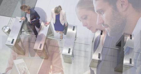 Image of diverse colleagues using laptops in office over commuters walking through turnstiles. business and communication technology concept digitally generated image.の写真素材