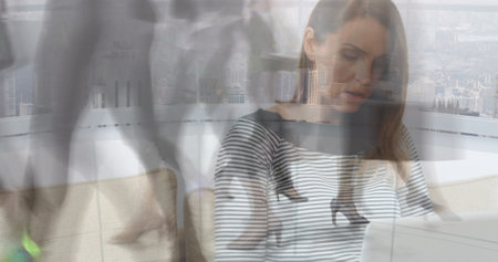 Image of woman working on laptop at home over sped up commuters walking in modern building. business and communication technology concept digitally generated image.の写真素材