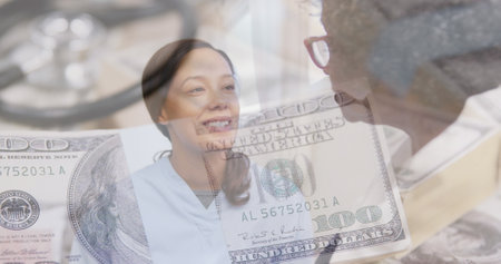 Image of stethoscope and american dollar bills over female doctor with senior woman talking. global coronavirus pandemic, medicine and healthcare concept digitally generated image.の写真素材