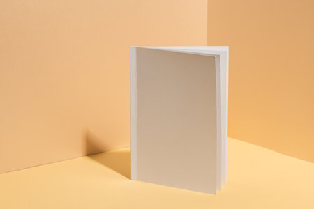 A blank white book stands open against a beige background with copy space. Ideal for showcasing cover designs, the image emphasizes the potential for customization.の写真素材