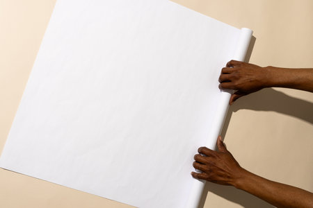 Hands unroll a blank white paper on a table, with copy space. The image captures a moment of...