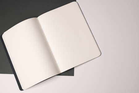 An open blank notebook lies on a dual-tone surface, with copy space. Ideal for a minimalist design, the image evokes creativity and planning in a home or office setting.の写真素材