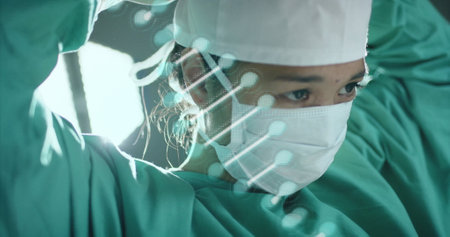 Image of dna strand over asian female surgeon in hospital. Global medicine, healthcare, connections, computing and data processing concept digitally generated image.の写真素材