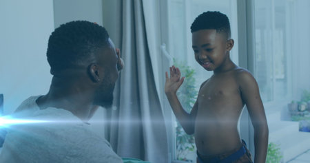 Image of lights over happy african american father and son undressing and clapping hands. family, togetherness, spending quality time concept digitally generated image.の写真素材