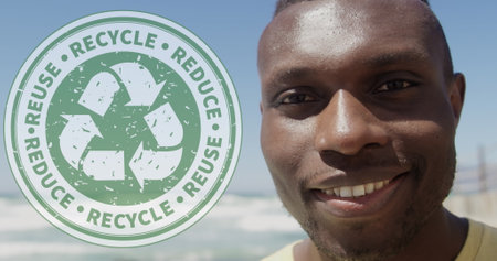 Image of recycling logo over portrait of smiling african american man at beach. eco conservation volunteer month digitally generated image.の写真素材
